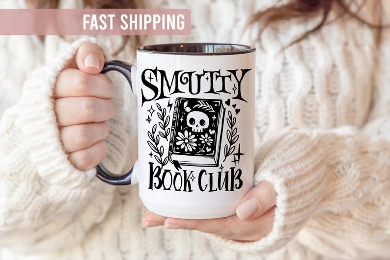 K&ouml;nnte beinhalten: Wei&szlig;er Keramikbecher mit schwarzem Henkel und Rand, mit dem Schriftzug "SMUTTY BOOK CLUB" in gotischer Schrift. Das Design umfasst ein Buch mit einem Totenkopf, Blumen und dekorativen Elementen.