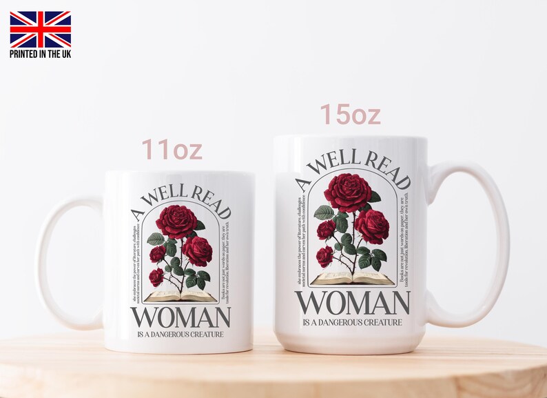 May include: Two white ceramic mugs, 11oz and 15oz, with a floral design. The design features red roses, an open book, and the text "A WELL READ WOMAN IS A DANGEROUS CREATURE". The mugs have a curved handle and are set on a wooden surface.