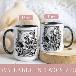 Puede incluir: Dos tazas de cer&aacute;mica blanca con asas y bordes negros. Cada taza presenta una ilustraci&oacute;n en blanco y negro de un esqueleto leyendo un libro, rodeado de elementos florales. El texto "THE READER" est&aacute; en la parte inferior. Disponibles en 312 ml y 425 ml.
