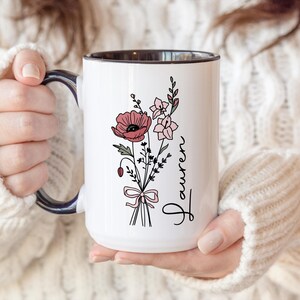 May include: A white ceramic mug with a black handle and the text "But First, Coffee" in a bold, black font. The mug is set against a blurred background, suggesting a cozy setting.