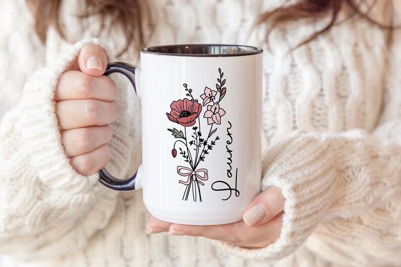May include: A white ceramic mug with a black handle and the text "But First, Coffee" in a bold, black font. The mug is set against a blurred background, suggesting a cozy setting.