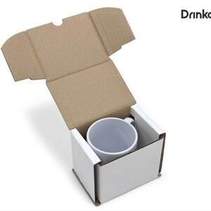 May include: A white ceramic mug inside a white cardboard box with a brown cardboard lid. The mug is centered in the box, and the lid is open. The text "Drinkably" is in the upper right corner.