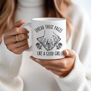 May include: White ceramic mug with the text "SPREAD THOSE PAGES LIKE A GOOD GIRL" in black. The mug features a black illustration of hands opening a book, with roses on either side. A perfect gift for book lovers.