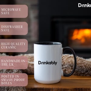 May include: A white ceramic mug with a black handle and rim, featuring the word "Drinkably" in black. The mug is labeled as microwave and dishwasher safe, made of high-quality ceramic, and handmade in the UK.