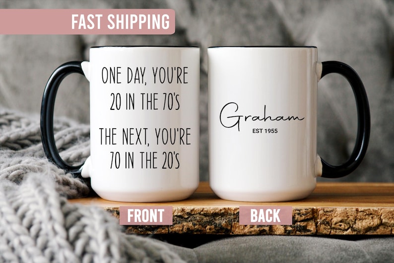 Puede incluir: Taza de cer&aacute;mica blanca con asa y borde negros. La parte delantera de la taza tiene el texto "ONE DAY, YOU'RE 20 IN THE 70'S THE NEXT, YOU'RE 70 IN THE 20'S". La parte trasera de la taza tiene el nombre "Graham" y "EST 1955".