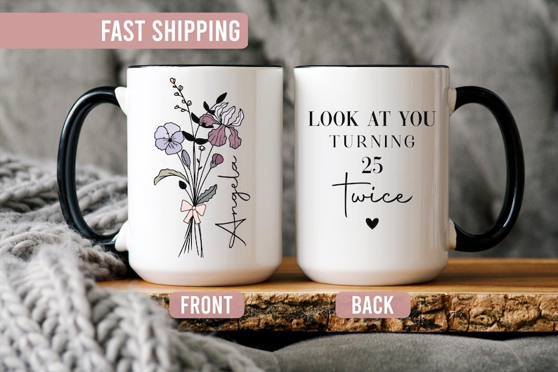 May include: A white ceramic mug with a black handle and rim. The front features a floral bouquet illustration with the name Angela. The back displays the black text LOOK AT YOU TURNING 25 twice with a small heart symbol below the lettering.