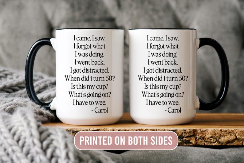 May include: Two white ceramic mugs with black handles, each printed with humorous text. The text reads "I came, I saw, I forgot what I was doing..." and is attributed to "Carol". The mugs are displayed on a wooden surface.