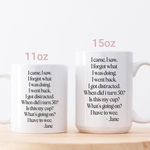 May include: Two white ceramic mugs, 11oz and 15oz, with a humorous quote printed in black. The text includes phrases like "I came, I saw, I forgot what I was doing." The mugs are on a light wooden surface.
