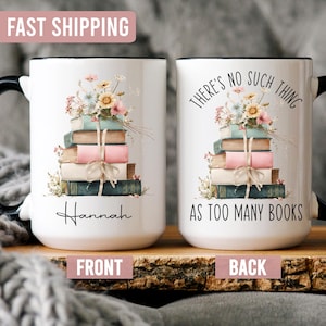 May include: White ceramic mug with a black handle and rim, featuring a stack of books adorned with flowers. The front of the mug has the name "Hannah" and the back says "THERE'S NO SUCH THING AS TOO MANY BOOKS."