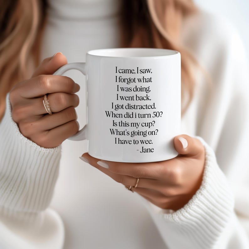 May include: White ceramic mug held by a person, featuring black text: "I came, I saw. I forgot what I was doing... When did I turn 50? Is this my cup? What's going on? I have to wee. - Jane."