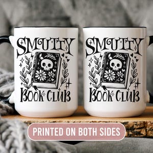 K&ouml;nnte beinhalten: Zwei wei&szlig;e Keramikbecher mit schwarzen Henkeln und R&auml;ndern. Jeder Becher tr&auml;gt die Aufschrift "Smutty Book Club" mit einem Totenkopf- und Blumenbuch-Design. Der Text "Printed on Both Sides" ist ebenfalls sichtbar.