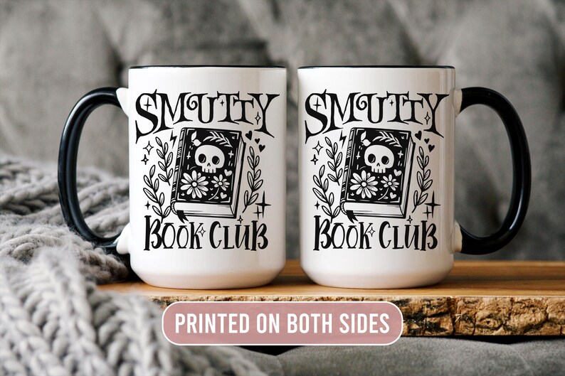 K&ouml;nnte beinhalten: Zwei wei&szlig;e Keramikbecher mit schwarzen Henkeln und R&auml;ndern. Jeder Becher tr&auml;gt die Aufschrift "Smutty Book Club" mit einem Totenkopf- und Blumenbuch-Design. Der Text "Printed on Both Sides" ist ebenfalls sichtbar.