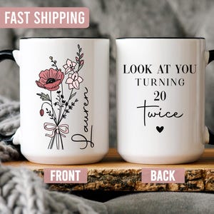 May include: White ceramic mug with a black handle and rim. One side features a floral bouquet with a pink poppy and the name "Lauren". The other side says "Look at you turning 20 twice" with a heart symbol.