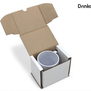 May include: A white ceramic mug inside a white cardboard box with a brown cardboard lid. The mug is centered in the box, and the lid is open. The text "Drinkably" is in the upper right corner.