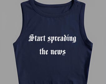 Op de afbeelding: Marineblauwe crop top met de witte tekst "Start spreading the news" in gotische letters. De mouwloze top heeft een ronde hals en is gemaakt van een zacht materiaal.