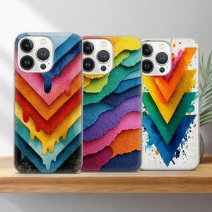 May include: Three phone cases with colorful, abstract designs. The cases feature layered, textured patterns in rainbow hues, with one showcasing dripping paint effects. The cases are displayed on a wooden shelf.