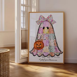 Può includere: Una stampa d'arte da parete incorniciata raffigurante un personaggio fantasma coperto da un motivo a patchwork colorato con un grande fiocco floreale sopra. Il fantasma tiene in mano un secchiello a forma di zucca arancione. Testo "Guty Green Staven.com" in basso.