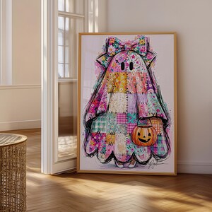 May include: A framed wall art print featuring a ghost character covered in a colourful patchwork quilt pattern with various floral and plaid designs. The ghost wears a large matching bow on its head and carries a small orange jack-o'-lantern bucket.