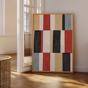May include: A rectangular wall art piece featuring a vertical striped pattern in a textured finish. The design consists of alternating blocks of red, black, light blue, beige, and off-white colors, all enclosed within a simple light wood frame.