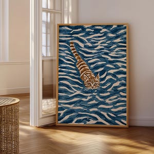 Könnte beinhalten: Ein rechteckiger gerahmter Wandkunstdruck, der eine braune getigerte Katze zeigt, die in tiefblauem und weißem Wasser schwimmt. Die Katze ist mittig platziert, wobei Kopf und gestreifter Schwanz über der stilisierten, welligen Wasseroberfläche.