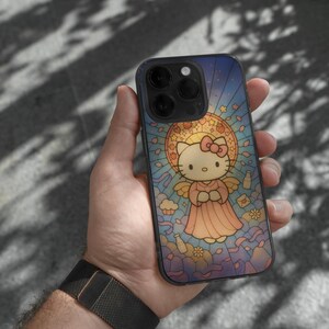 May include: A smartphone case with a stained-glass effect, depicting Hello Kitty as an angel. The design features a blue and yellow backdrop with a pink bow and dress. The phone case is held in a person's hand.