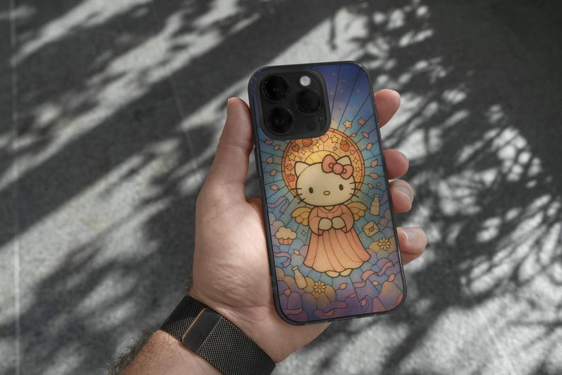 May include: A smartphone case with a stained-glass effect, depicting Hello Kitty as an angel. The design features a blue and yellow backdrop with a pink bow and dress. The phone case is held in a person's hand.