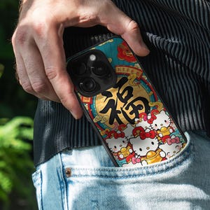 May include: A smartphone case with a vibrant design featuring Hello Kitty characters and Chinese calligraphy. The case, held in a pocket, displays a teal, gold, and red colour scheme. The design includes the Chinese character for "blessing".