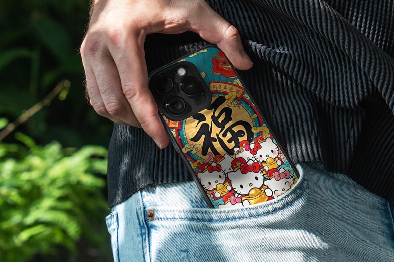May include: A smartphone case with a vibrant design featuring Hello Kitty characters and Chinese calligraphy. The case, held in a pocket, displays a teal, gold, and red colour scheme. The design includes the Chinese character for "blessing".
