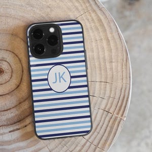 May include: A smartphone case with a striped pattern in shades of blue and white. The case features a circular design with the initials "JK" in light blue. The case is black around the camera lenses.