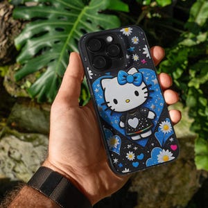May include: Black phone case with a Hello Kitty design. The case has a black background with white daisies and stars. Hello Kitty is wearing a black dress with a white heart and a blue bow. The case is held in a hand.