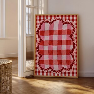 May include: A rectangular framed wall art piece featuring a red and white gingham background pattern. Centered on the print is a large, cloud-shaped motif with a pink and red gingham fill, outlined by a scalloped dark red border.