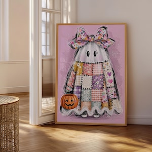 May include: A framed wall art print featuring a ghost character with a large floral bow on its head. The ghost is wearing a patchwork-style dress with various floral and plaid patterns in pink, purple, and white, and is holding an orange jack-o'-lantern.