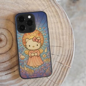 May include: A black phone case with a stained-glass effect, depicting Hello Kitty as an angel. The design includes a halo, wings, and a pink dress against a blue backdrop. The phone case is on a wooden surface.