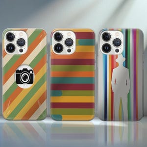 Op de afbeelding: Drie telefoonhoesjes met kleurrijke ontwerpen. Eén hoesje heeft diagonale strepen en een camera-afbeelding. Een andere heeft horizontale strepen in verschillende kleuren. De derde heeft een wit silhouet op verticale strepen.
