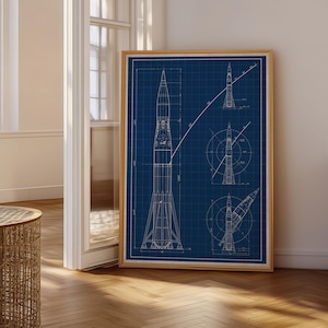 May include: A framed blueprint art print featuring a dark blue background with white technical line drawings of a rocket. The design includes a large central vertical rocket view, two smaller circular cross-section diagrams, and one angled rocket view.