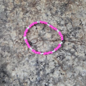 May include: A beaded bracelet featuring bright pink and silver beads. The bracelet is circular and appears to be made of small, evenly spaced beads. The beads are strung together to form a flexible band.