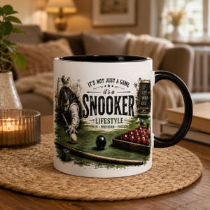May include: A white ceramic mug with a black interior and handle, featuring a graphic of a snooker player, a cue, balls, and a rack. The text reads: IT'S NOT JUST A GAME it's a SNOOKER LIFESTYLE FOCUS PRECISION PASSION and EAT SLEEP SNOOKER REPEAT.