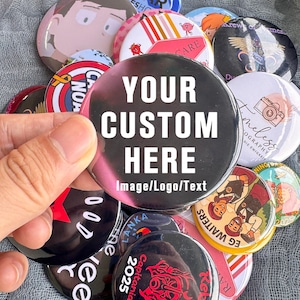 May include: A collection of colorful custom buttons with various designs and text. One button prominently displays "YOUR CUSTOM HERE" and "Image/Logo/Text". Other buttons feature illustrations, logos, and text, including "CARE", "EG WAITERS", and "Capitania 2025".