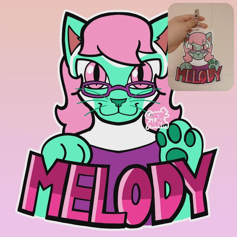 May include: A cartoon cat character with teal fur, pink hair, and glasses. The cat is wearing a purple shirt and has the name "MELODY" in large pink letters below. A smaller version of the character is shown as a keychain.