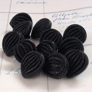 Può includere: Un gruppo di dieci bottoni in plastica nera con un design a coste. I bottoni sono disposti in un gruppo su una superficie bianca.