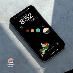 May include: A black smartphone displays a space-themed wallpaper with planets and a person on a boat. The time is 8:52, with the date Thursday, November 20th. The phone has a black case and the text "Wallpapers Central."