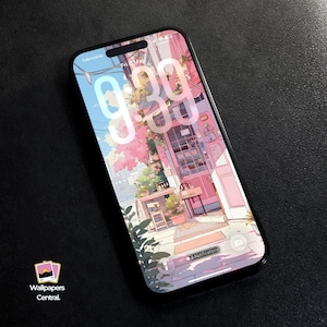 May include: A smartphone displays a digital wallpaper with a pink and blue anime-style street scene. The time 9:39 is visible on the screen. The phone has a black frame and is on a dark surface. The wallpaper features a shop with a table and chairs.