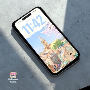 May include: A black smartphone displays a scenic wallpaper with a church steeple, buildings, and trees. The time 11:42 is visible on the screen. The phone is on a gray surface. The logo for Wallpapers Central is in the lower left corner.