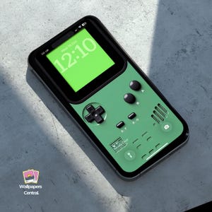 Puede incluir: Una funda de teléfono verde y negra diseñada para parecerse a una consola de juegos portátil retro. La funda presenta un panel direccional, botones y una pantalla que muestra la hora. La funda del teléfono está sobre una superficie gris.