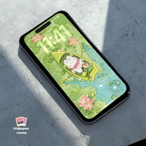 May include: A smartphone displays a whimsical wallpaper featuring a cartoon mouse in a boat on a pond with lily pads and flowers. The time, 11:41, is visible at the top. The phone is black with a gray surface background.