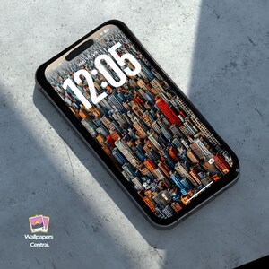 May include: A black smartphone displays a cityscape wallpaper with a time of 12:05. The phone is angled, showing a detailed view of the buildings. The phone is on a gray surface. The logo for Wallpapers Central is in the lower left corner.