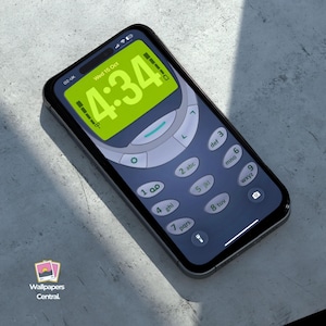 May include: A smartphone with a screen displaying a retro phone interface. The screen shows the time 4:34 in a green digital font. The phone has a black frame and a keypad design.