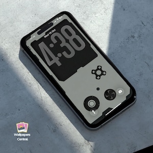May include: A smartphone with a black case displays a retro video game controller design on its screen. The screen shows the time 4:38 in large numbers. The phone is on a light gray surface.