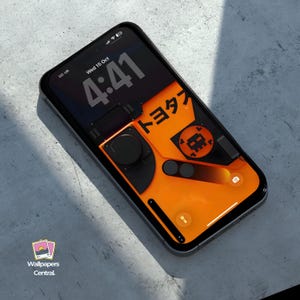 Puede incluir: Un smartphone muestra un fondo de pantalla digital con un diseño negro y naranja. El fondo de pantalla presenta caracteres japoneses y una estética retro-futurista. La hora es 4:41. El teléfono está sobre una superficie gris claro.