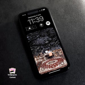 May include: A black smartphone displays a wallpaper with a dark, abstract design and a person at a desk. The time is 11:39 AM, Wednesday, June 4th. The phone has a black case and the logo "Wallpapers Central" is visible.